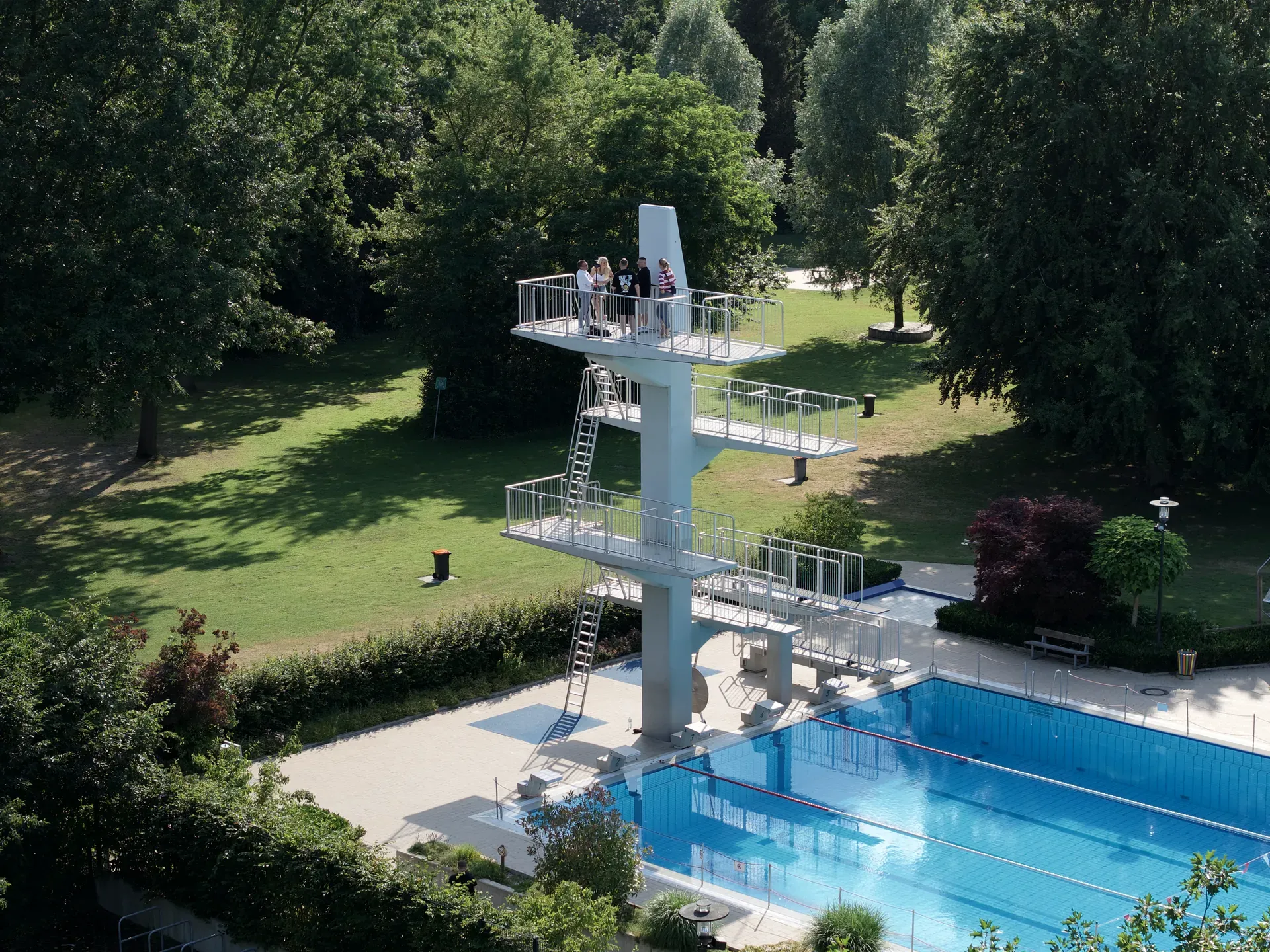 Drohnenaufnahme vom Werbedreh für das Anna Beatz Open Air 2026: Team auf dem 10-Meter-Sprungturm über dem Becken des Freibads Verl