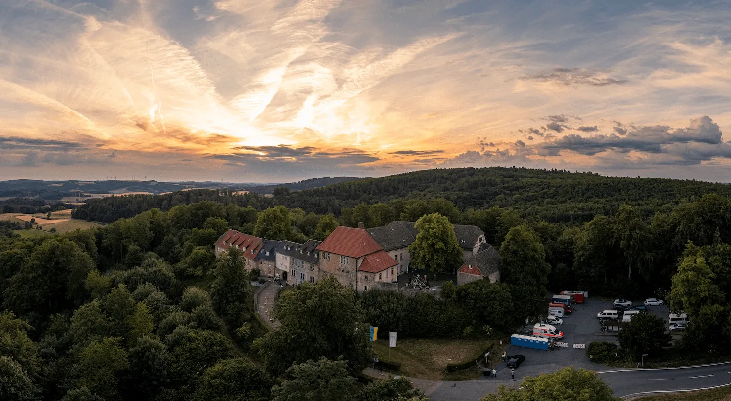Drohnenaufnahme eines Gutshofs im Abendlicht vor bewaldeten Hügeln