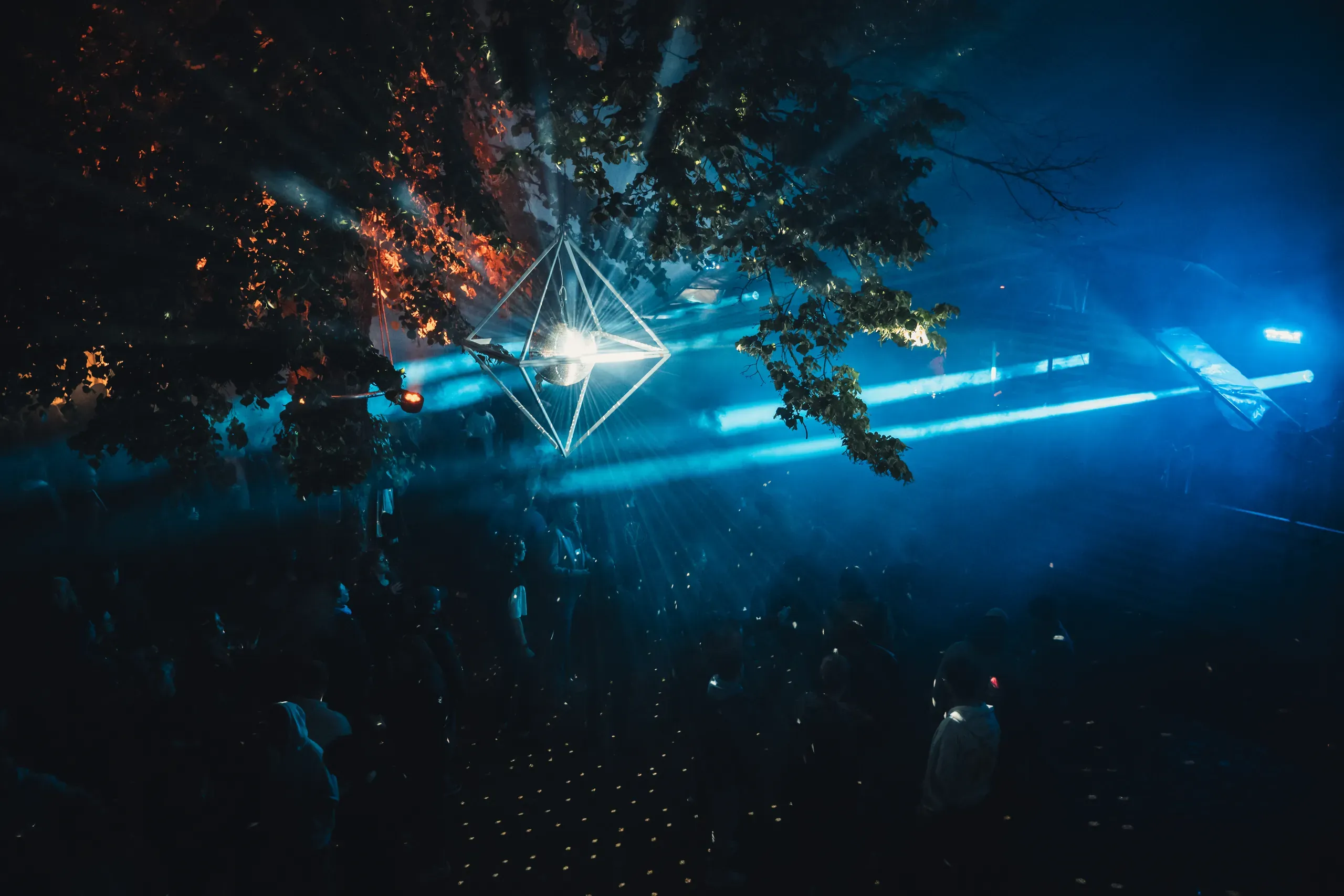 Lichtshow mit blauen Strahlen über dem Publikum unter alten Bäumen beim Burgbeben 2025 auf der Burg Sternberg
