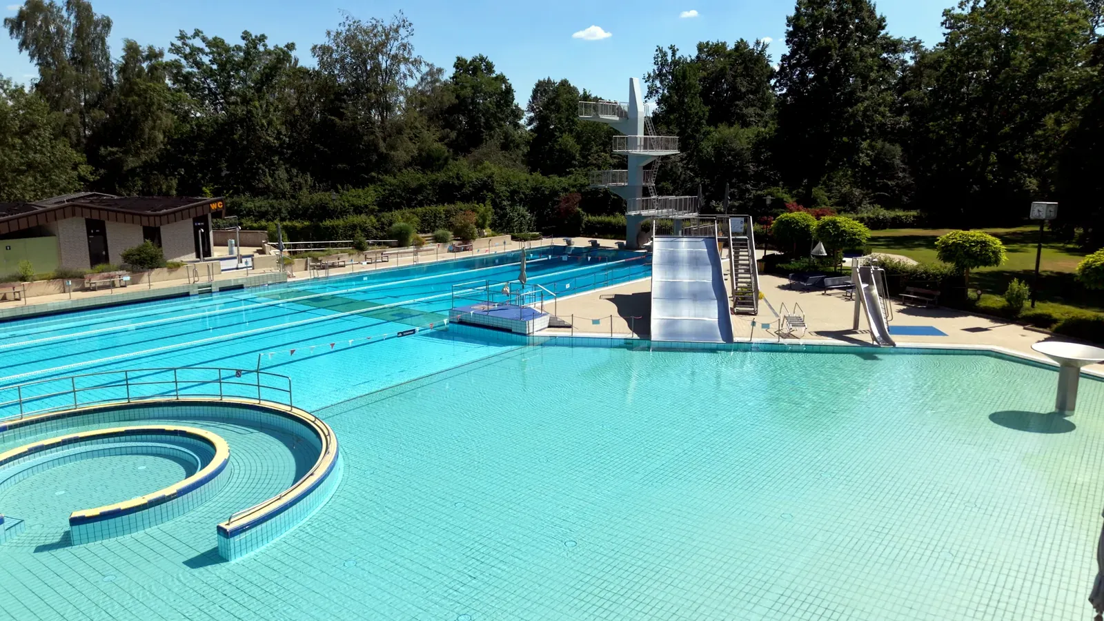 Freibad Verl: Becken mit Sitzstufen, Rutsche und Sprungturm im Sonnenlicht