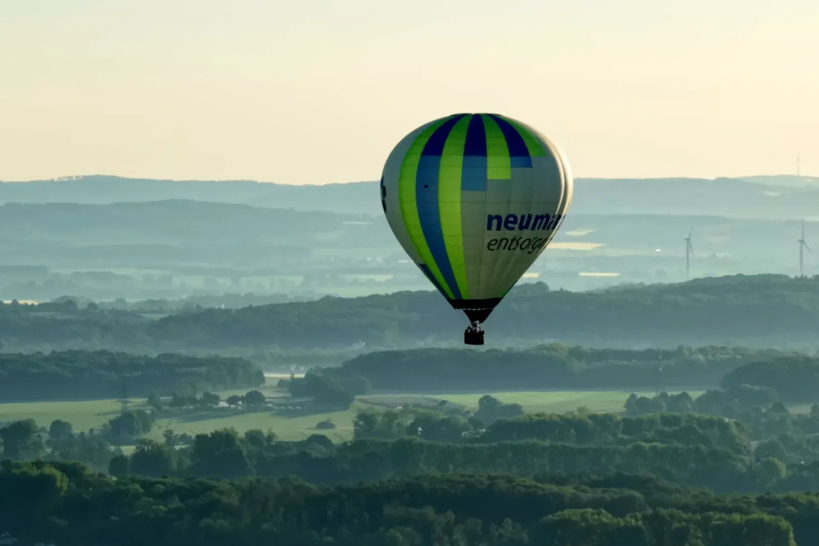 Heißluftballon bei Sonnenaufgang über dem Lipperland bei Lage, dahinter Windräder und Hügelketten im Morgendunst