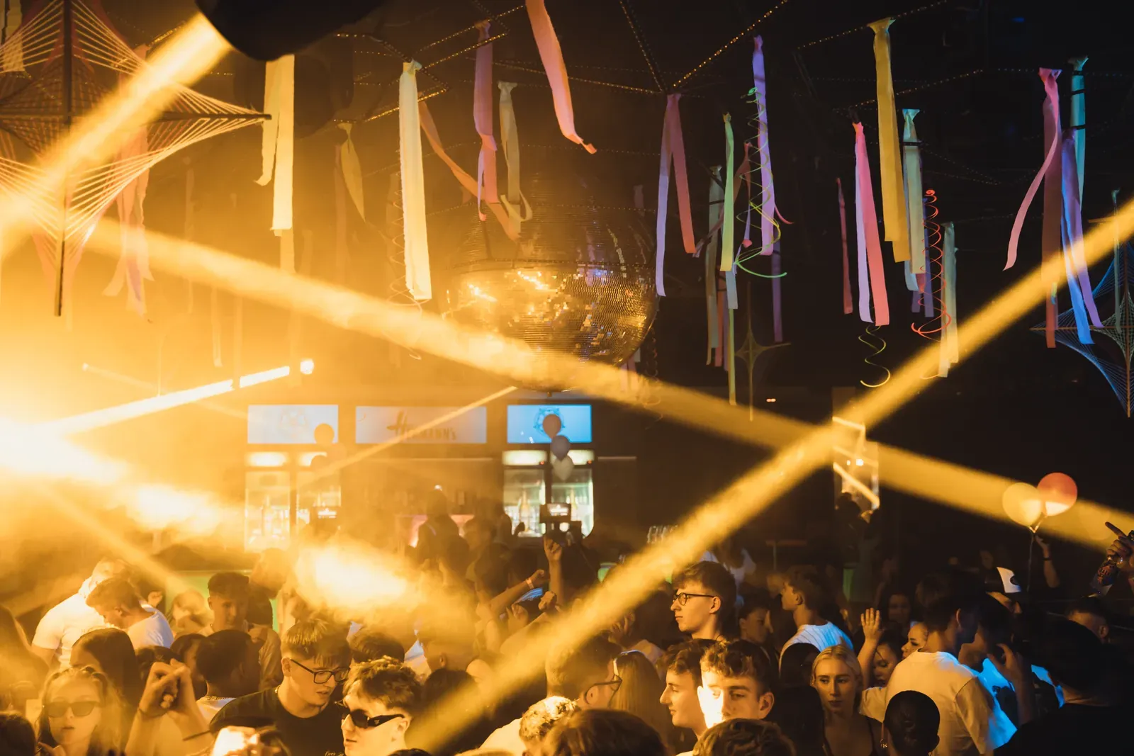 Gelbe Lichtstrahlen über der feiernden Menge im Hermanns Club