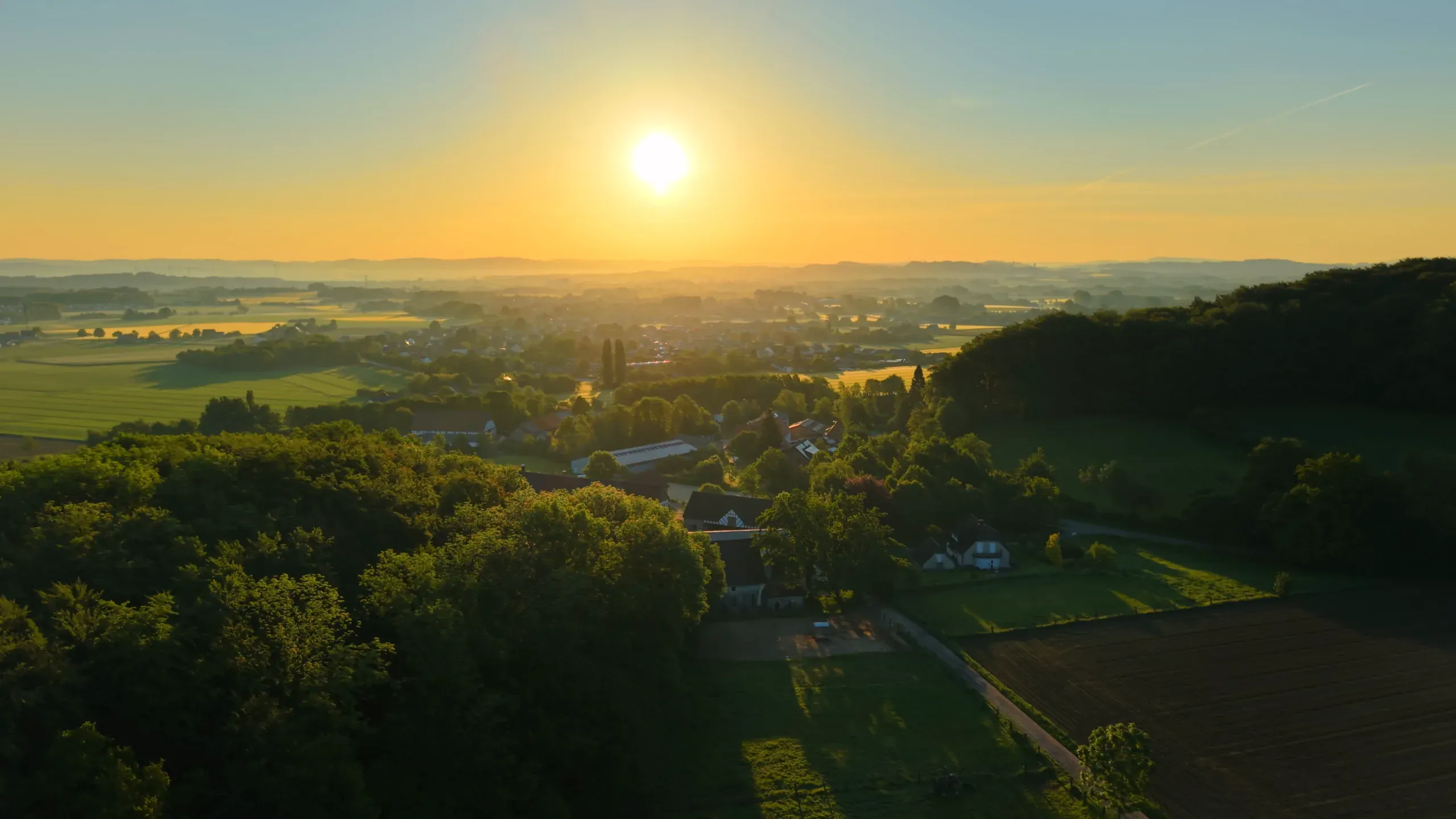 Luftaufnahme bei Sonnenaufgang über dem Lipperland: Felder, Höfe und Waldkuppen im Morgendunst